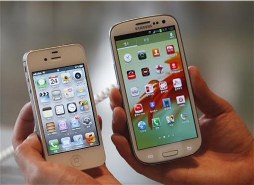 An employee poses as he holds Apple's iPhone 4s and Samsung's Galaxy S III at a store in Seoul