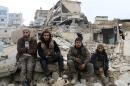 Rebel fighters sit on the rubble of damaged buildings as they wait to be evacuated from a rebel-held sector of eastern Aleppo