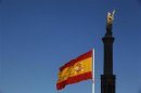 A Spanish flag flutters in the wind near a statue of Columbus in Madrid