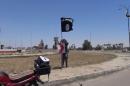 An image grab taken from a video uploaded on May 18, 2015 by Aamaq News Agency, a Youtube channel that posts videos from areas under the Islamic State (IS) group's control, allegedly shows an IS fighter hanging the group's flag in Ramadi, Iraq