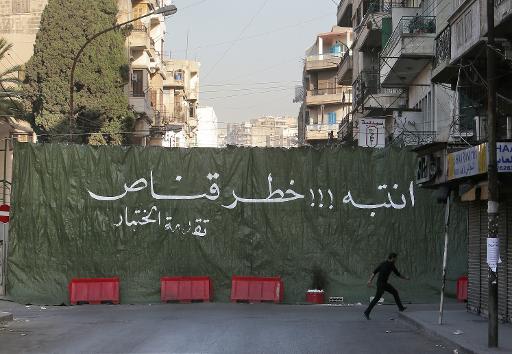 A man runs in front of a curtain reading: "Danger of sniper" in a street in Zahriyeh, at the southern entrance of Tripoli's Bab al-Tabbaneh Sunni area during clashes with the Alawite, pro-Syrian President Bashar al-Assad, on December 2, 2013