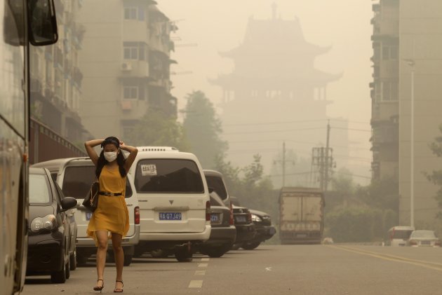 A woman wears a mask as she walks along a street in front of a Chinese temple during a hazy day in Wuhan, Hubei province June 11, 2012. China's carbon emissions could be nearly 20 percent higher than previously thought, a new analysis of official Chinese data showed on Sunday, suggesting the pace of global climate change could be even faster than currently predicted. REUTERS/Stringer (CHINA - Tags: ENVIRONMENT) CHINA OUT. NO COMMERCIAL OR EDITORIAL SALES IN CHINA