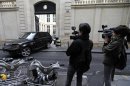 Journalists work as a car and scooter drive away from the home of French businessman Bernard Tapie in Paris
