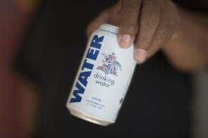 A resident holds a can of water donated by the Anheuser-Busch &hellip;