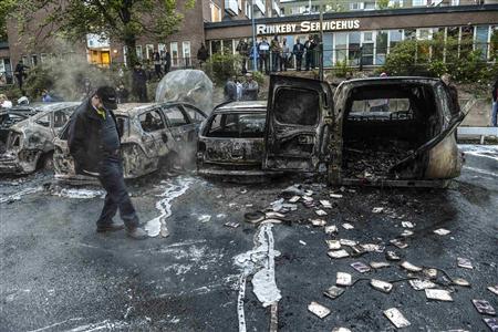 A bystander checks the debris around a row of burnt cars in the suburb of Rinkeby after youths rioted in several different suburbs around Stockholm May 23, 2013. REUTERS/Fredrik Sandberg/Scanpix