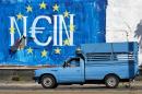 A man drives his van past a graffiti made by street artist N_Grams that read ''NO'' in German but also ''YES, IN'' in Greek language in Athens, on Sunday, June 28, 2015. Greece's parliament voted early Sunday in favor of Prime Minister Alexis Tsipras' motion to hold a July 5 referendum on creditor proposals for reforms in exchange for loans.(AP Photo/Petros Giannakouris)