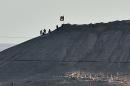 Alleged Islamic State group militants stand next to an IS flag atop a hill in the Syrian town of Ain al-Arab, known as Kobane by the Kurds, as seen from the Turkish-Syrian border in the southeastern town of Suruc on October 6, 2014
