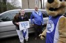 In this Tuesday, March 15, 2016 photo, Maya Wolf, 17, left, holds a sign to her mother, not shown, from the driveway of their home in Franklin, Mass., as she is visited by Wheaton College President Dennis Hanno, center, and the school's mascot. Wolf was presented with an acceptance letter from Wheaton College officials during the visit. More colleges have started to hand-deliver portions of their acceptance letters to students. (AP Photo/Steven Senne)