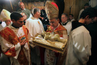Latin Patriarch of Jerusalem Fouad Twal, center, holds the Baby Jesus as he and clergy arrive to pray at the Grotto, traditionally believed by Christians to be the birthplace of Jesus Christ, at the Church of the Nativity, in the West Bank town of Bethlehem, early Tuesday, Dec. 25, 2012. (AP Photo/Abed Al Hashlamoun, Pool)