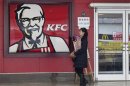 A woman walks past a KFC restaurant as a logo of McDonald is reflected on a door window, in Wuhan