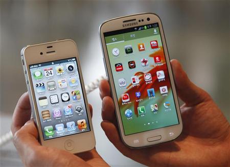 An employee poses as he holds Apple's iPhone 4s and Samsung's Galaxy S III at a store in Seoul
