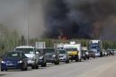 A convoy of evacuees drives south as flames and smoke rises along the highway near near Fort McMurray, Alberta on May 6, 2016
