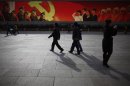 People walk in front of a screen showing propaganda displays near the Great Hall of the People at Beijing's Tiananmen Square