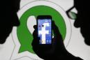 An illustration photo shows a man holding a smart phone with a Facebook logo as its screen wallpaper in front of a WhatsApp messenger logo, in Zenica