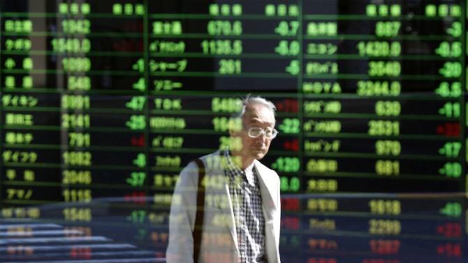 A pedestrian is reflected in an electronic board displaying various stock prices at a brokerage in Tokyo