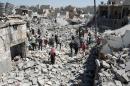 Syrians stand on the rubble of buildings after a missile fired by government forces hit a residential area in the Maghayir district of Aleppo on July 21, 2015