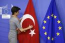 A woman adjusts the Turkish flag next to the EU flag before the arrival of Turkish PM Davutoglu at the EU Commission headquarters in Brussels
