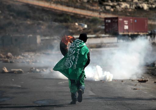 A Palestinian protestor wearing a flag from the Hamas Islamic movement holds a burning tyre during clashes in the West Bank village of Betunia on November 27, 2013