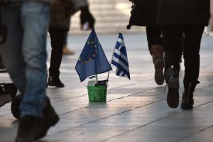 People walk next to a Greek and an EU flag in Athens …