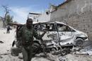 Somali government soldiers walks next to car damaged from explosion near Al Mukaram hotel in Mogadishu