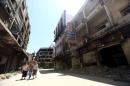 Women walk past damaged buildings along a street in the old city of Homs
