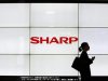 A woman walks past the Sharp Corp's Logo at a train station in Tokyo