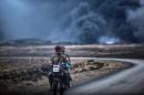An Iraqi soldier and a civilian ride a motorbike as smoke rises behind them, on the road between Qayyarah and Mosul on October 28, 2016