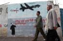 Yemeni men walk past a mural depicting a drone and reading, " Why did you kill my family?" on December 13, 2013 in Sanaa