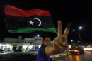 A man, with an inked finger, flashes the victory sign as he celebrates with the new Libyan flag at the end of voting day in Sirte