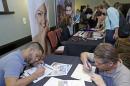 In this Wednesday, Oct. 22, 2014 photo, job seekers Stevens de la Pena, foreground left, and Eduardo Perez, foreground right, fill out a job application at a job fair in Miami Lakes, Fla. The Labor Department releases weekly jobless claims on Wednesday, Nov. 26, 2014. (AP Photo/Alan Diaz)