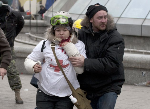 In this Thursday, Feb. 20, 2014 photo, Olesya Zhukovska, left, is helped after being shot in her neck by a sniper bullet, in Independence Square, the epicenter of the country's current unrest, Kiev, Ukraine. “I am dying,” Olesya Zhukovska, a 21-year-old volunteer medic, wrote on Twitter, minutes after she got shot in the neck by a sniper’s bullet as deadly clashes broke out in the center of the Ukrainian capital between protesters and police. The tweet, accompanied by a photo of her clutching her bleeding neck and being led away under fire, went viral, as social media users around the world presumed she had died and shared their grief and anger. But Zhukovska survived. She has become a symbol of the three-month protest of President Viktor Yanukovych’s government and a movement for closer ties with the West and human rights. (AP Photo/Alexander Sherbakov)