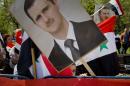 A child of the Syrian community in Romania peers from behind a picture of Syrian President Bashar Assad, during a rally in Bucharest, Romania, Sunday, April 9, 2016. Syrians gathered in a protest against foreign support for the rebel groups in Syria and voiced their support for the country's president Bashar Assad and his regime. (AP Photo/Vadim Ghirda)