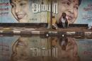 A flood-affected couple sits along a flooded roadside under a picture of Jayalalithaa, CM of Tamil Nadu, in Chennai