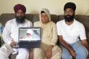 Raghuvinder Singh, left, and Jaspreet Singh, right, pose with their mother, Kulwant Kaur, and a photograph of their father, Punjab Singh, on Friday, Aug. 1, 2014, at Jaspreet Singh's home in Oak Creek, Wisconsin. Punjab Singh was severely wounded in a mass shooting at his Sikh temple in 2012, and his family says his lifelong teachings of optimism and hope have sustained them through his long, slow recovery. (AP Photo/Dinesh Ramde)