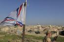 A Dwekh Nawsha militia member stands next to a flag of the Assyrian Patriotic Party, as he stands guard on the rooftop of a building in the Christian village of Bakufa, 30 kilometers (18.6 miles) north of Mosul, Iraq, Wednesday, Nov. 12, 2014. The party flag has replaced the black flag of the Sunni militants of the Islamic State group and is waving on the roof of the building at the entrance to the village. (AP Photo/Bram Janssen)
