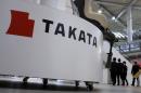 FILE PHOTO: Visitors walk behind a logo of Takata Corp on its display at a showroom for vehicles in Tokyo