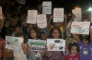 Syrian children hold up signs during a night demonstration at Sarmada on the outskirts of Idlib