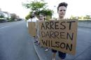 Protester Hana Kato, of Tacoma, Wash., holds a sign that reads "Arrest Darren Wilson" as she attends an evening rally Tuesday, Aug. 19, 2014, in Tacoma, Wash. Wilson has been identified as the police officer who fatally shot 18-year-old Michael Brown in Ferguson, Missouri, an event that has sparked nightly clashes between protesters and police. (AP Photo/Ted S. Warren)