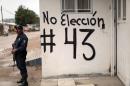 A Mexican police officer stands next to a wall with graffiti calling for a boycott of upcoming elections and asking for news on 43 missing students in Tlapa de Comonfort, Guerrero State, on June 4, 2015