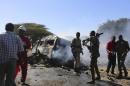 Somali government soldiers stand around the wreckage after a suicide car bomb explosion targeting peacekeeping troops in a convoy outside the capital Mogadishu