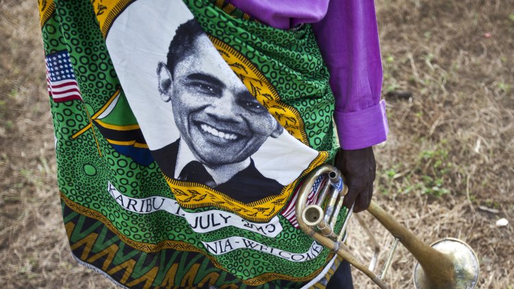 A member of the brass band that will welcome U.S. President Barack Obama stands on the road next to State House, wearing a shirt with the face of Obama, ahead of the meeting with Tanzanian President Jakaya Kikwete, at State House in Dar es Salaam, Tanzania Monday, July 1, 2013. The Democratic president was to fly Monday into Dar es Salaam, Tanzania, the last stop on a weeklong tour of Africa that wraps up Tuesday, while his Republican predecessor coincidentally also plans to be there for a conference on African women organized by the George W. Bush Institute. (AP Photo/Ben Curtis)