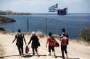 Syrian migrants walk past Greek and European flags as they head towards the town of Mithimna on Lesbos island, after arriving in an inflatable boat from Turkey on August 22, 2015