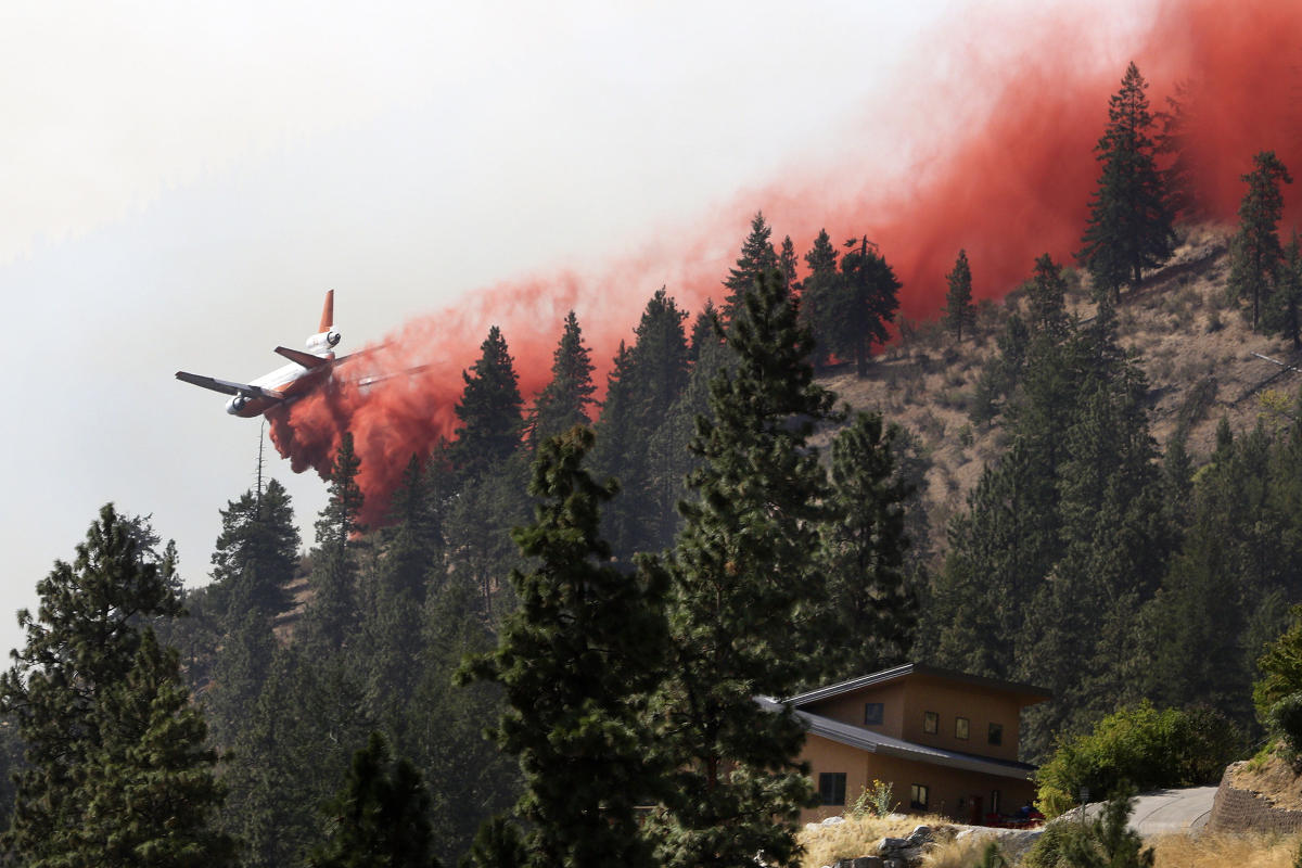A tanker airplane drops fire retardant on a hillside above a neighborhood on Lake Chelan in north-central Washington state as a wildfire blazes, Friday morning, Aug. 21, 2015. Massive wildfires expanding across the arid state have so overtaxed firefighters that the federal government declared an emergency and state officials took the unprecedented step of seeking volunteers to help fight the flames. (Genna Martin/The Herald via AP) MANDATORY CREDIT
