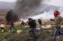 Palestinian protesters take cover from tear gas thrown by Israeli security forces during clashes following a demonstration against Israeli settlements in the West Bank village of Turmus Aya, north of Ramallah on December 19, 2014