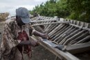 In this May 4, 2013 photo, a boat maker sharpens his machete which he will use to build a sailboat in Leogane, Haiti. The 30-foot-long boats, whose frames resemble the rib cage of a small dinosaur, are purchased by smugglers for around $12,000 and then taken to northern Haiti to find passengers. One boat builder said he has four or five regular customers. (AP Photo/Dieu Nalio Chery)