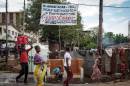 People walk in front of a banner warning against the deadly Ebola virus on October 4, 2014 in a street of Freetown