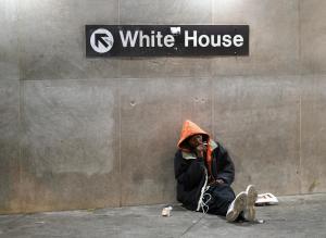 A homeless man sits under a sign giving directions &hellip;