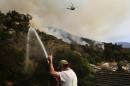 Mark Davis gives a thumbs-up toward a helicopter as he sprays water around his property, Thursday, Jan. 16, 2014, in Azusa, Calif. A wildfire burned out of control near homes in the dangerously dry foothills of the San Gabriel Mountains early Thursday, fanned by gusty Santa Ana winds that spit embers into neighborhoods in the city below, igniting trees. Evacuations were ordered for houses at the edge of the fire. (AP Photo/Jae C. Hong)