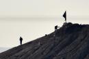 Alleged Islamic State (IS) militants stand next to a black IS flag atop a hill in the Syrian town of Ain al-Arab, known as Kobane by the Kurds, on October 7, 2014