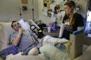 In this Thursday, May 9, 2013 photo, Marc Fucarile, left, jokes while speaking with members of the media as his fiancee, Jennifer Regan, right, looks on in his room at Massachusetts General Hospital in Boston. Fucarile was only feet away from a bomb blast Monday, April 15 near the finish line of the Boston Marathon that resulted in the loss of one leg, severe damage to the other, as well as burns, and a piece of shrapnel lodged in his heart. (AP Photo/Steven Senne)
